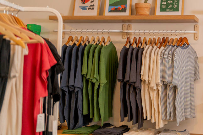 Clothing store interior with racks of clothes and shelves displaying bags.